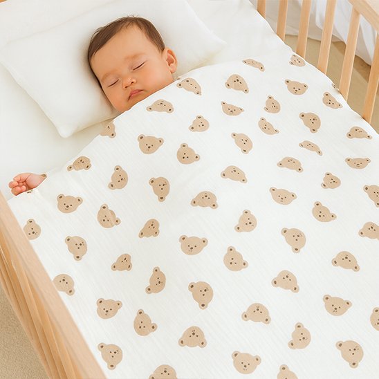 Bébé dans lit avec couverture visages oursons